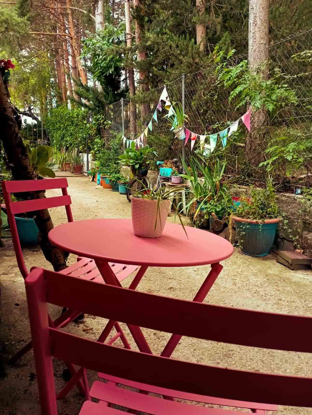 Una mesa y sillas de color rosa en un jardín con una planta en maceta encima.