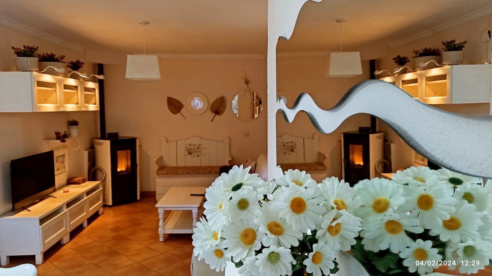 Una sala de estar con un jarrón de margaritas en primer plano.