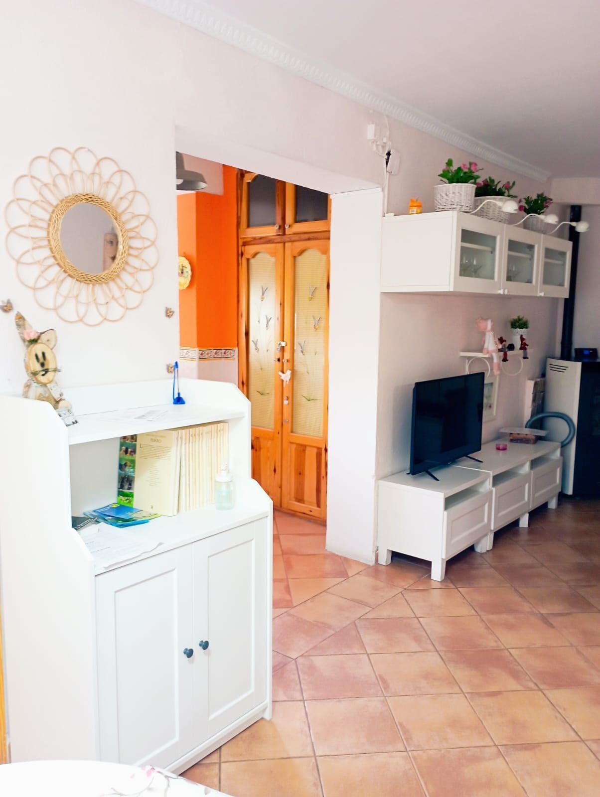 Una sala de estar con un televisor en un soporte y un espejo en la pared.