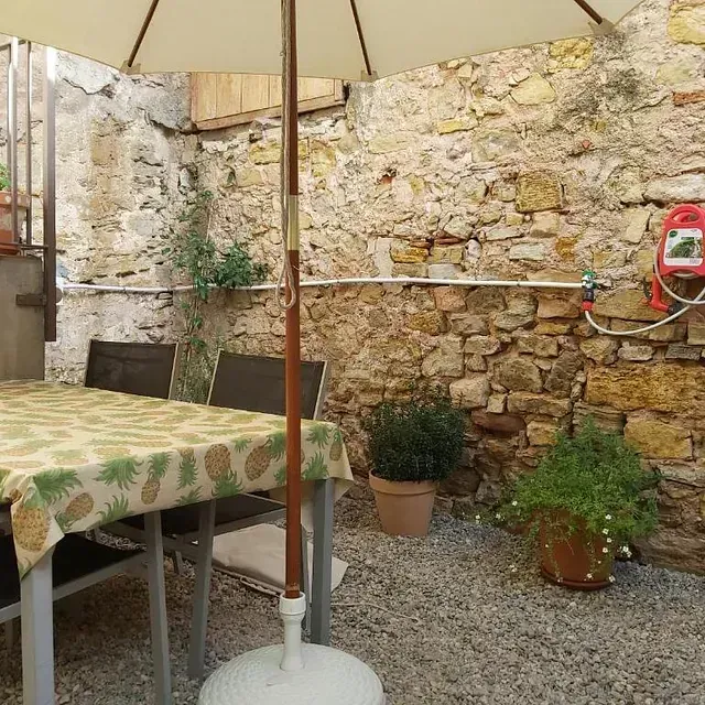 Una mesa y sillas bajo una sombrilla frente a un muro de piedra.