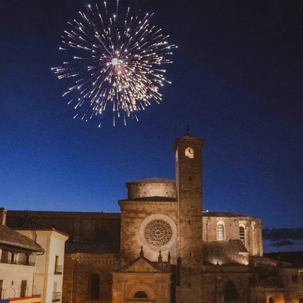 Se muestran fuegos artificiales sobre una iglesia con una torre de reloj.
