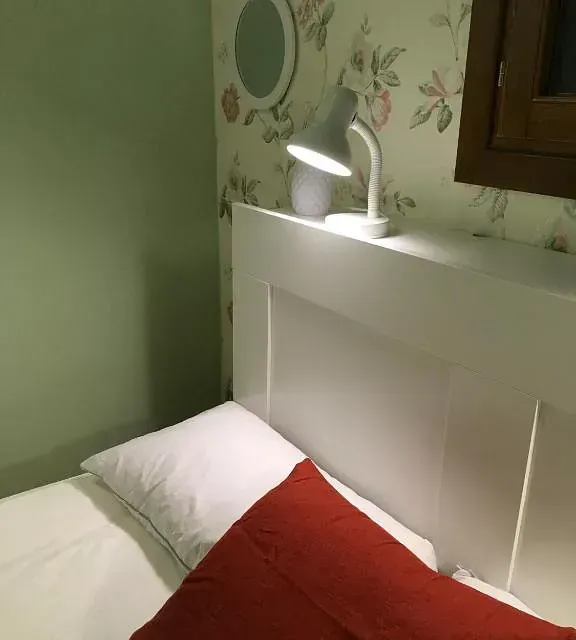 Una cama con una almohada roja y una lámpara en la cabecera.