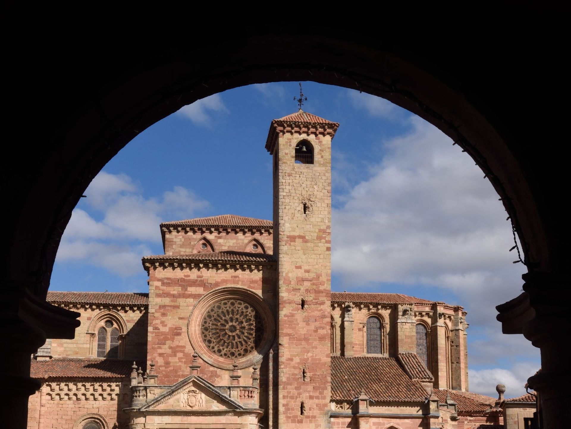 A través de un arco se ve un gran edificio de ladrillo con una torre de reloj.
