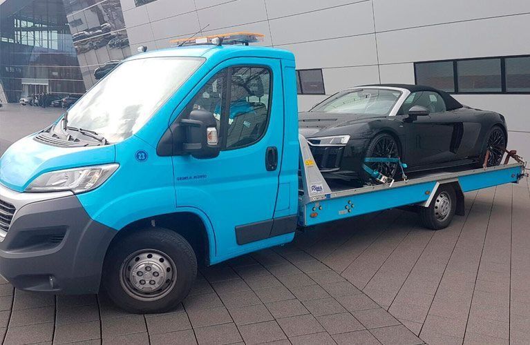 Una grúa azul lleva un coche negro en la parte trasera.