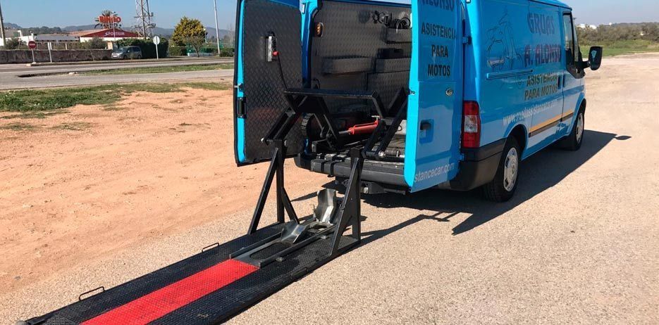 Una camioneta azul con una rampa adjunta está estacionada al costado de la carretera.
