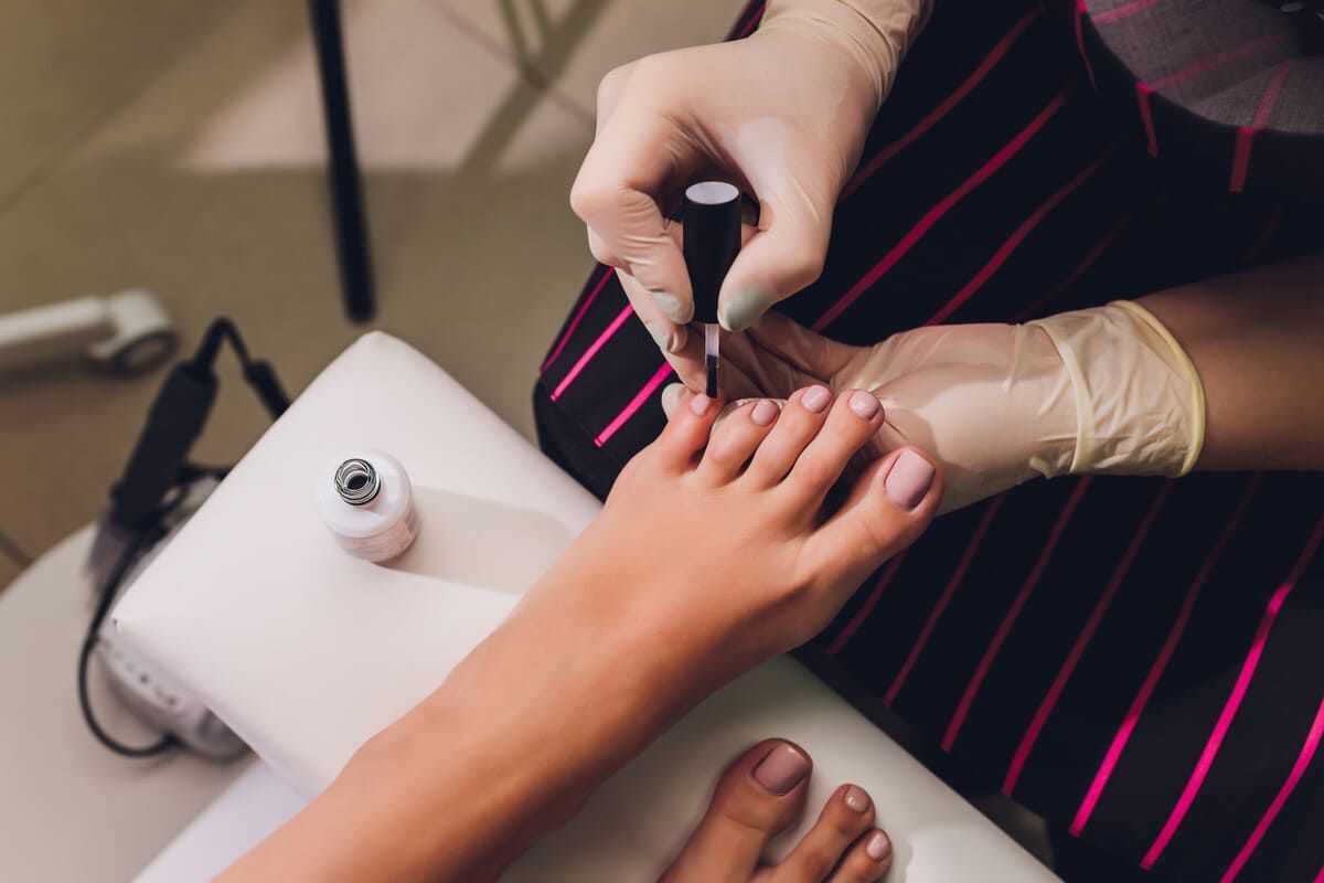 Manicurista aplicando esmalte de uñas en las uñas de los pies de una clienta; sesión de pedicura.