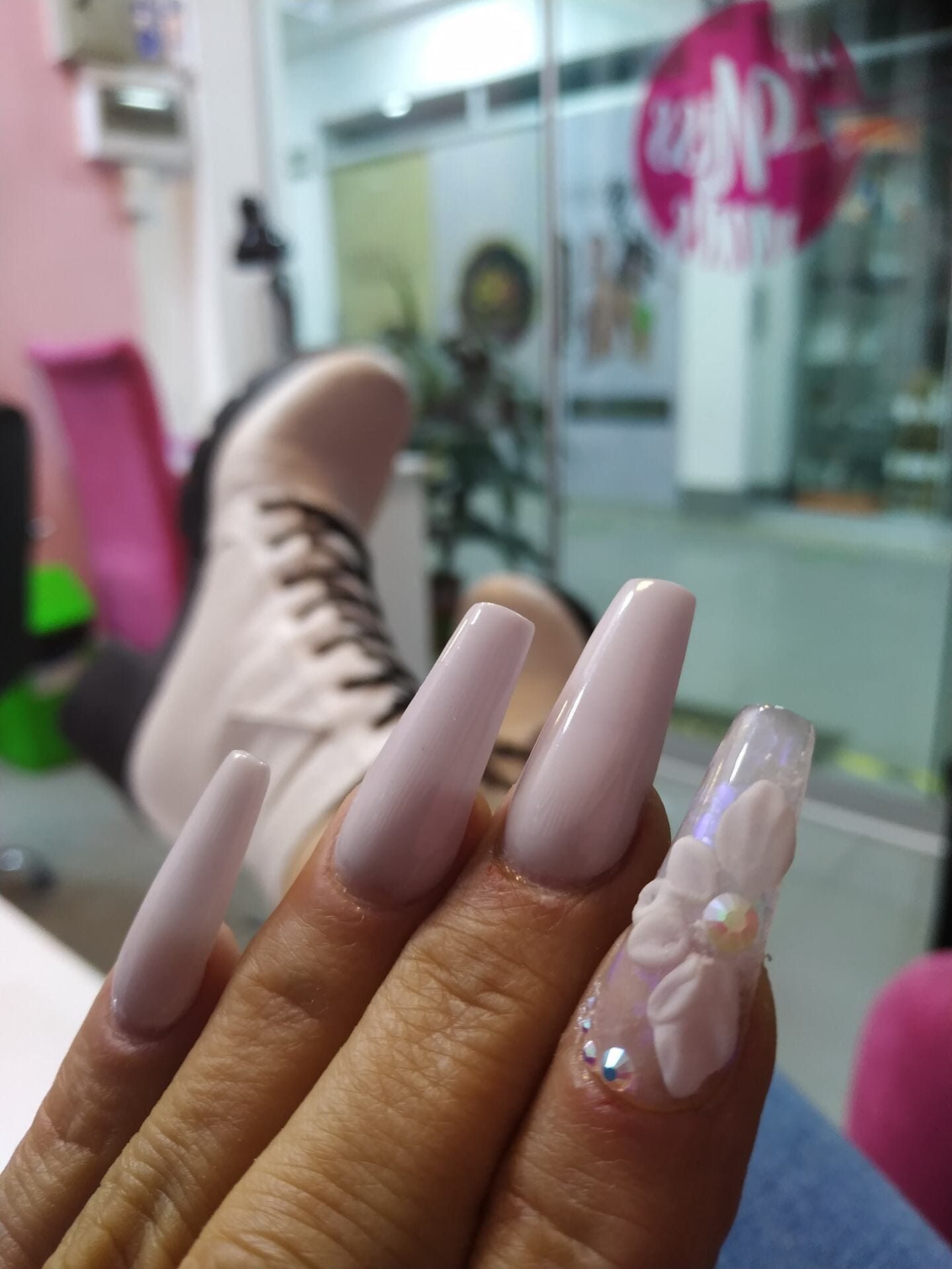 Primer plano de una mano con un diseño de uñas adornado: flores 3D rosas y burdeos, diamantes de imitación y acentos de gotas.