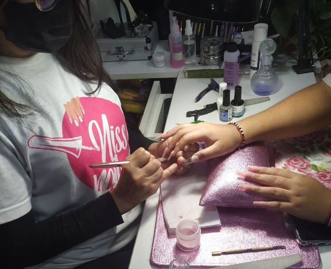 Mujer pintando las uñas de una clienta en un salón de manicura. Mesa con purpurina rosa y herramientas.