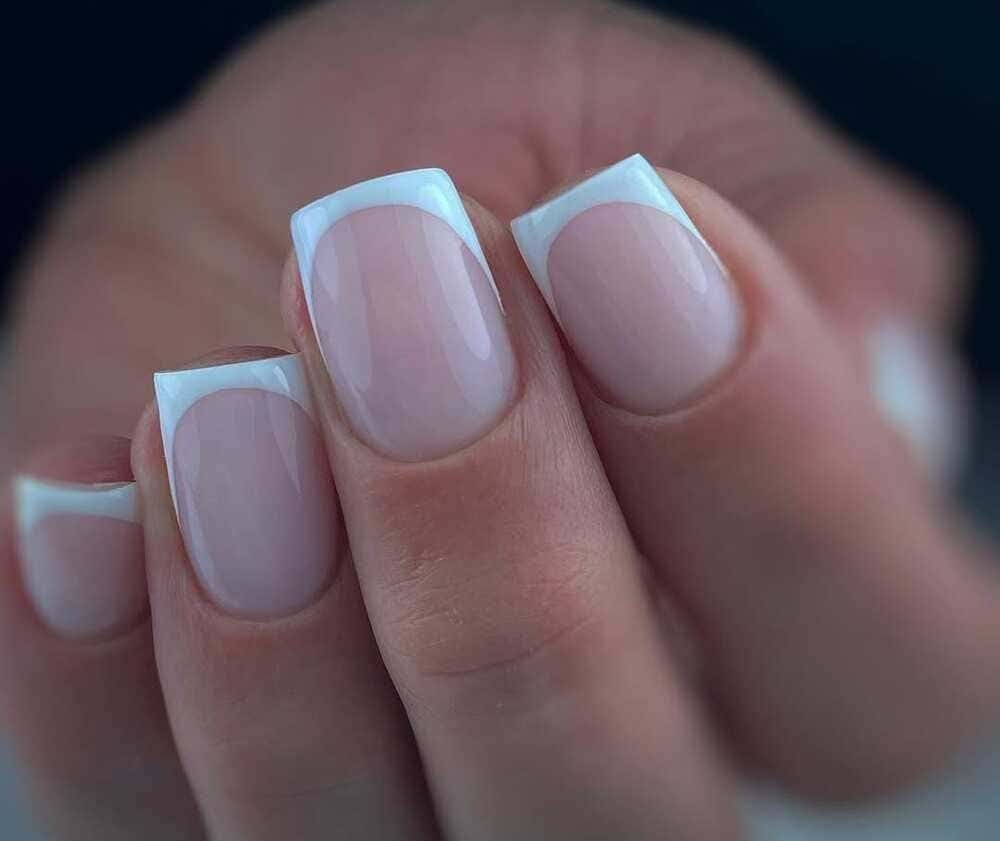 Mano con manicura francesa con punta cuadrada; uñas con puntas blancas y esmalte rosa pálido.