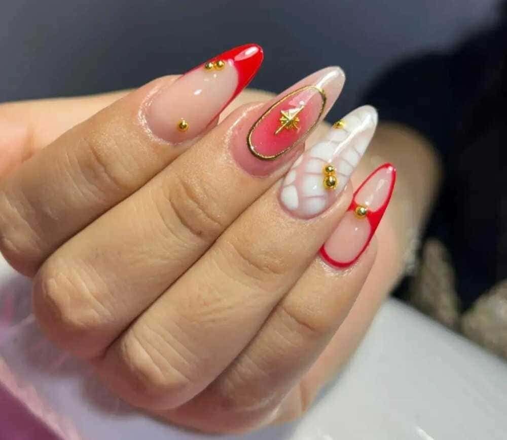 Mano con uñas largas y almendradas. Puntas rojas y transparentes, adornadas con detalles dorados y delicados diseños.