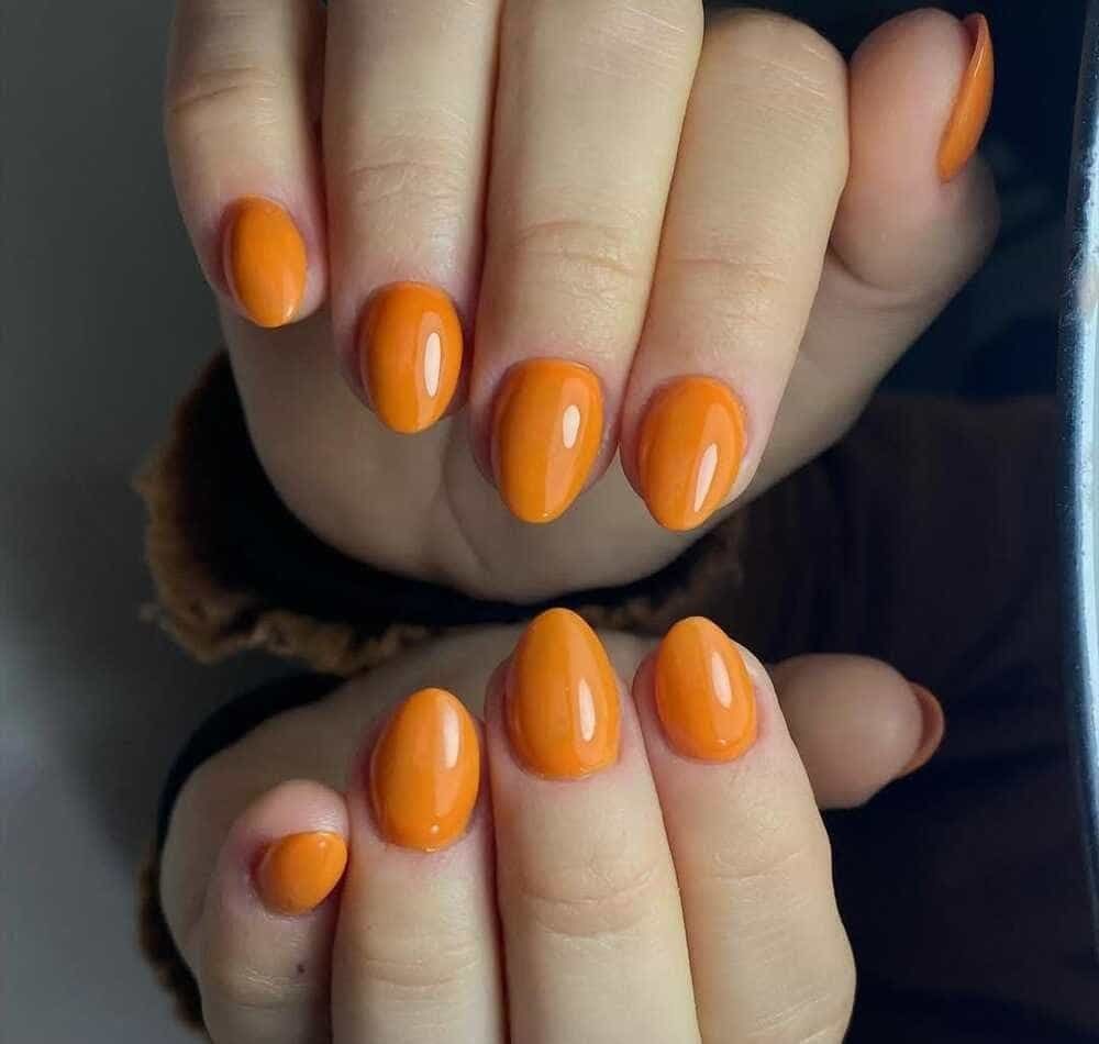 Manos con uñas de color naranja y forma ovalada.