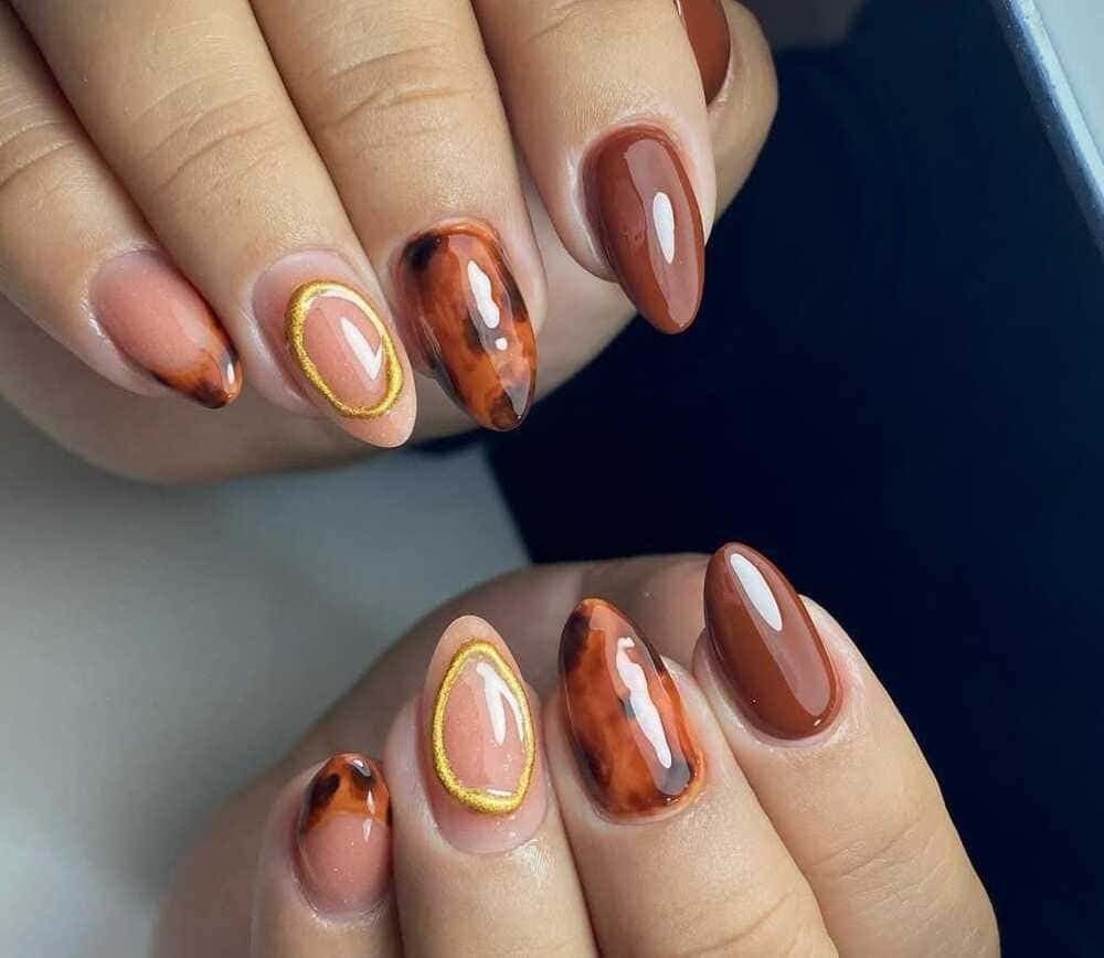 Manos con uñas en forma de almendra: diseños en tonos marrones, nude y carey con óvalos delineados en oro.