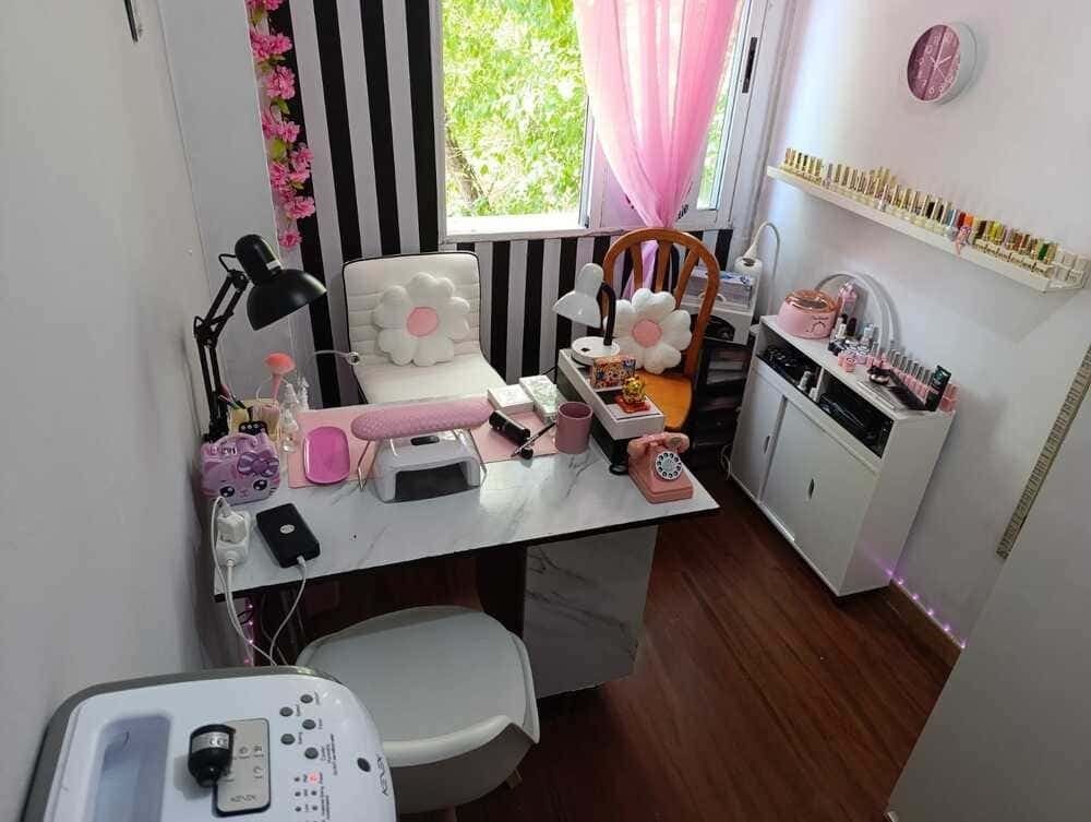 Estación de salón de uñas rosa y blanca con escritorio, herramientas y decoración floral.