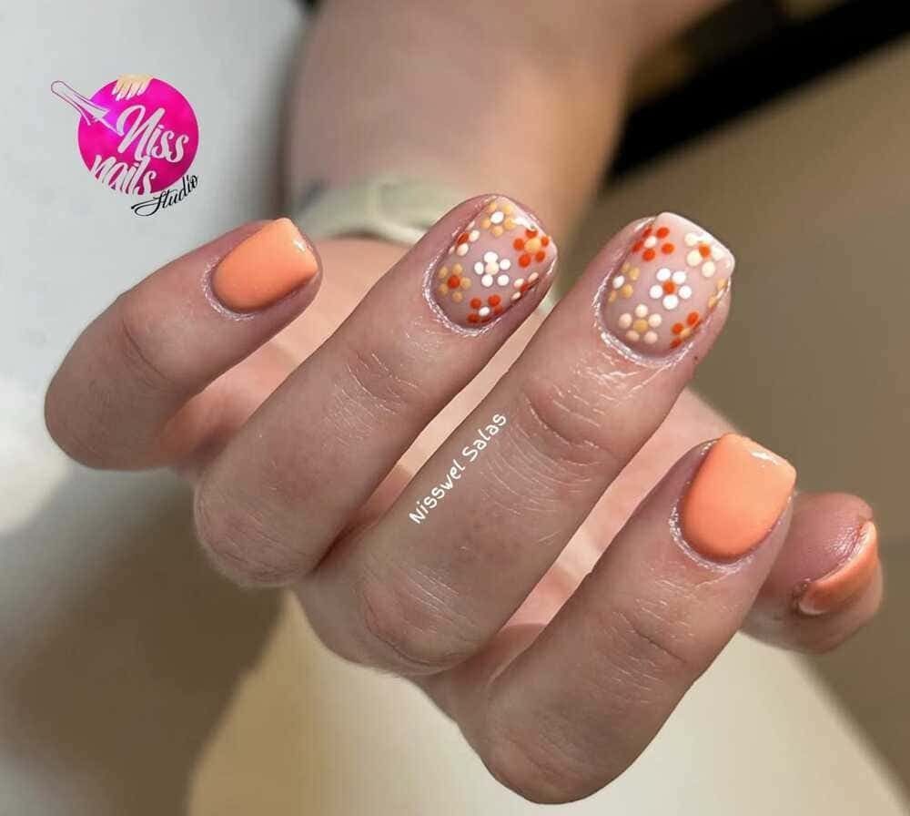 Mano con nail art naranja y floral.
