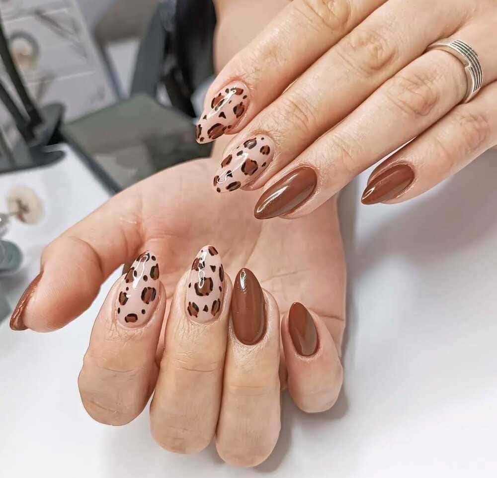 Manos con uñas almendradas, algunas con estampado de leopardo, otras de color marrón. Apoyadas sobre un escritorio.