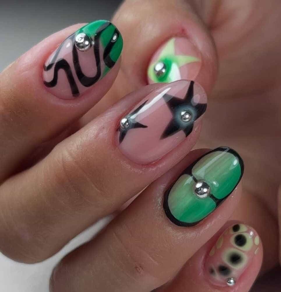 Primer plano de una mano con uñas ovaladas. Cada uña presenta diseños artísticos únicos con detalles en negro, verde, rosa y plata.