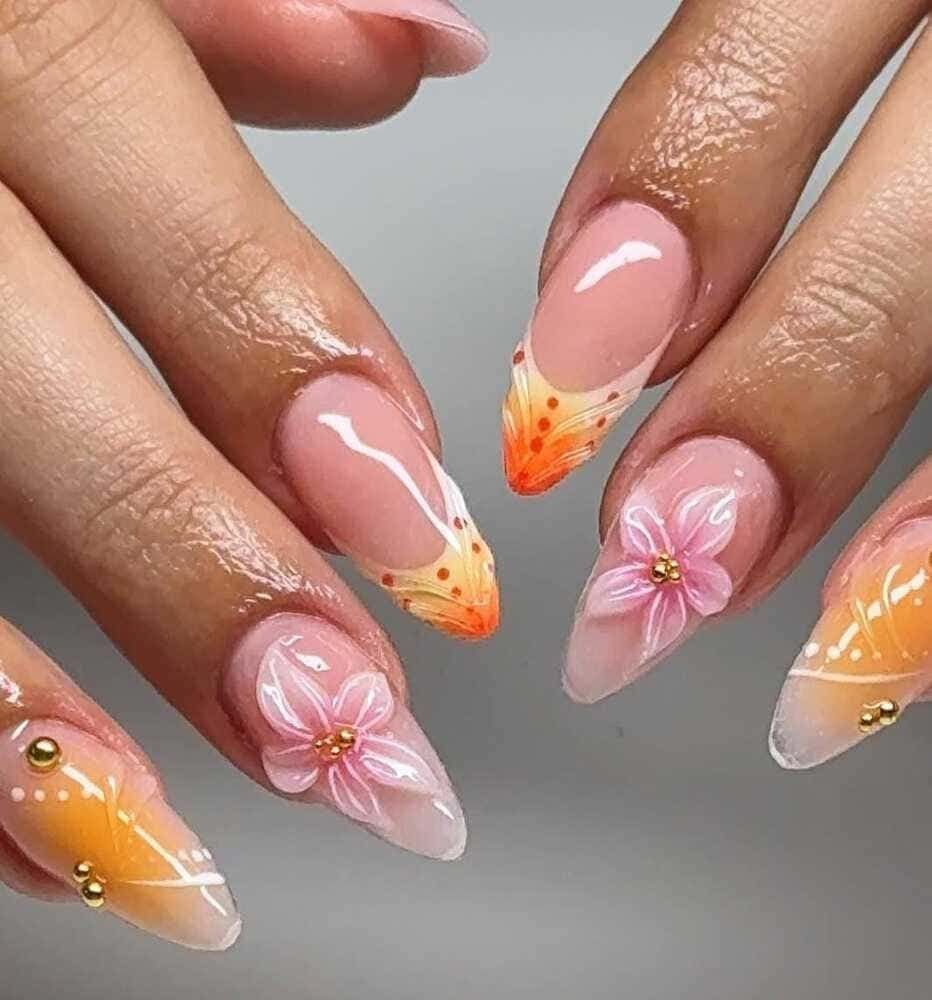 Primer plano de uñas cuidadas con varios diseños, incluidas flores en 3D, puntas francesas y colores naranja degradados.