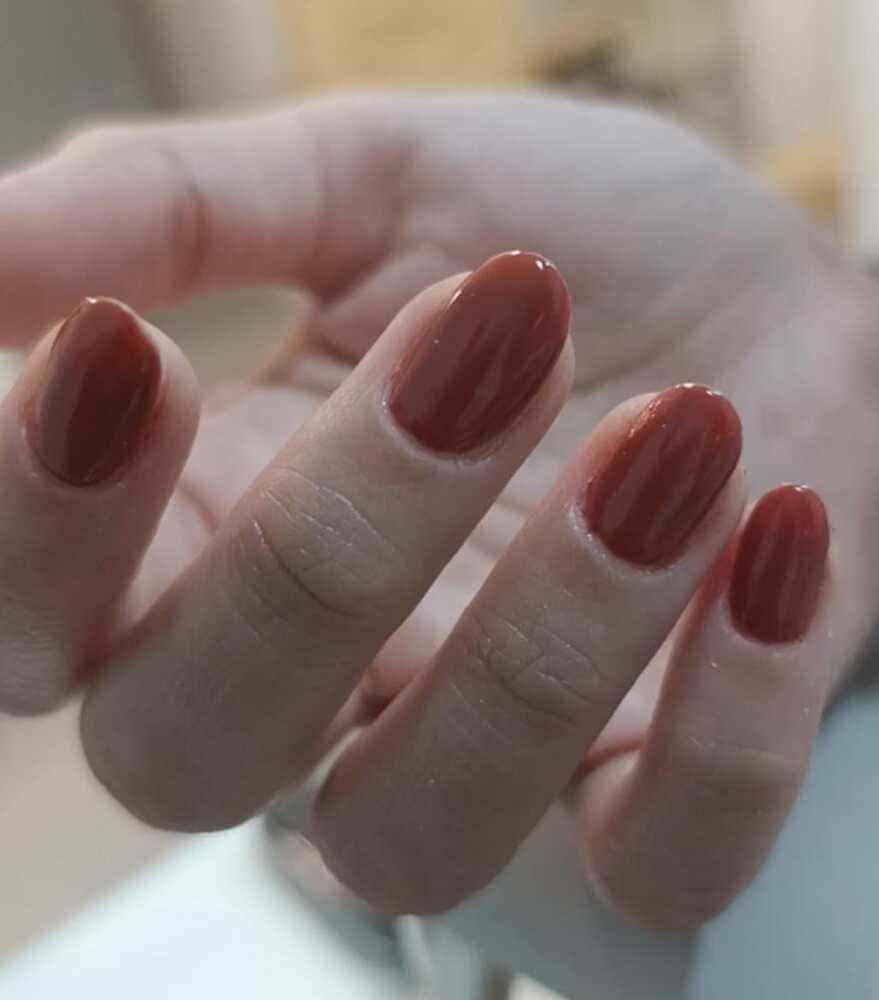Mano con uñas de forma ovalada pintadas de un cálido color marrón rojizo.