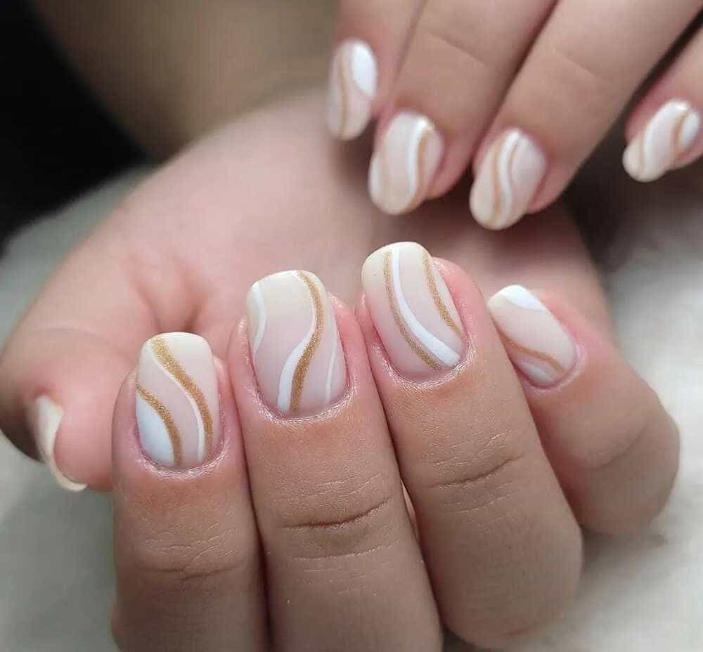 Uñas cuidadas con diseño ondulado beige y dorado.