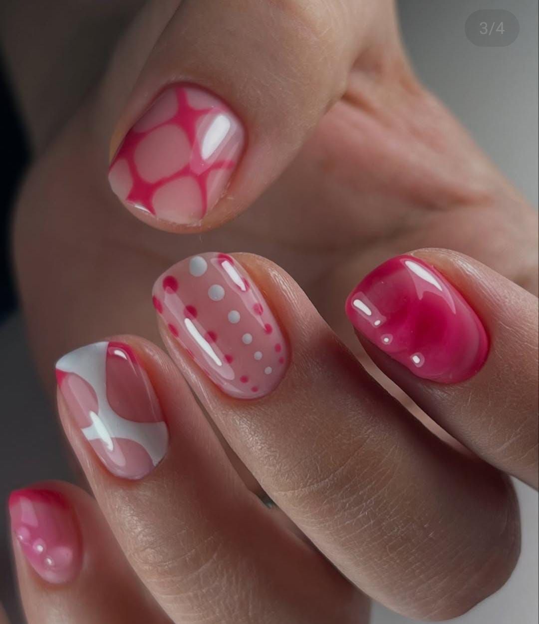 Mano con diseños de uñas cortas, rosas y blancas: formas abstractas, puntos y colores sólidos.