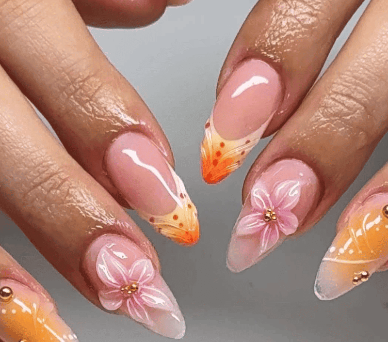 Primer plano de uñas cuidadas con diseños en blanco, durazno y naranja, incluidos detalles de flores y puntos.