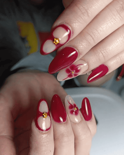 Primer plano de uñas cuidadas. Rojas y transparentes, con diseños florales y adornos dorados.