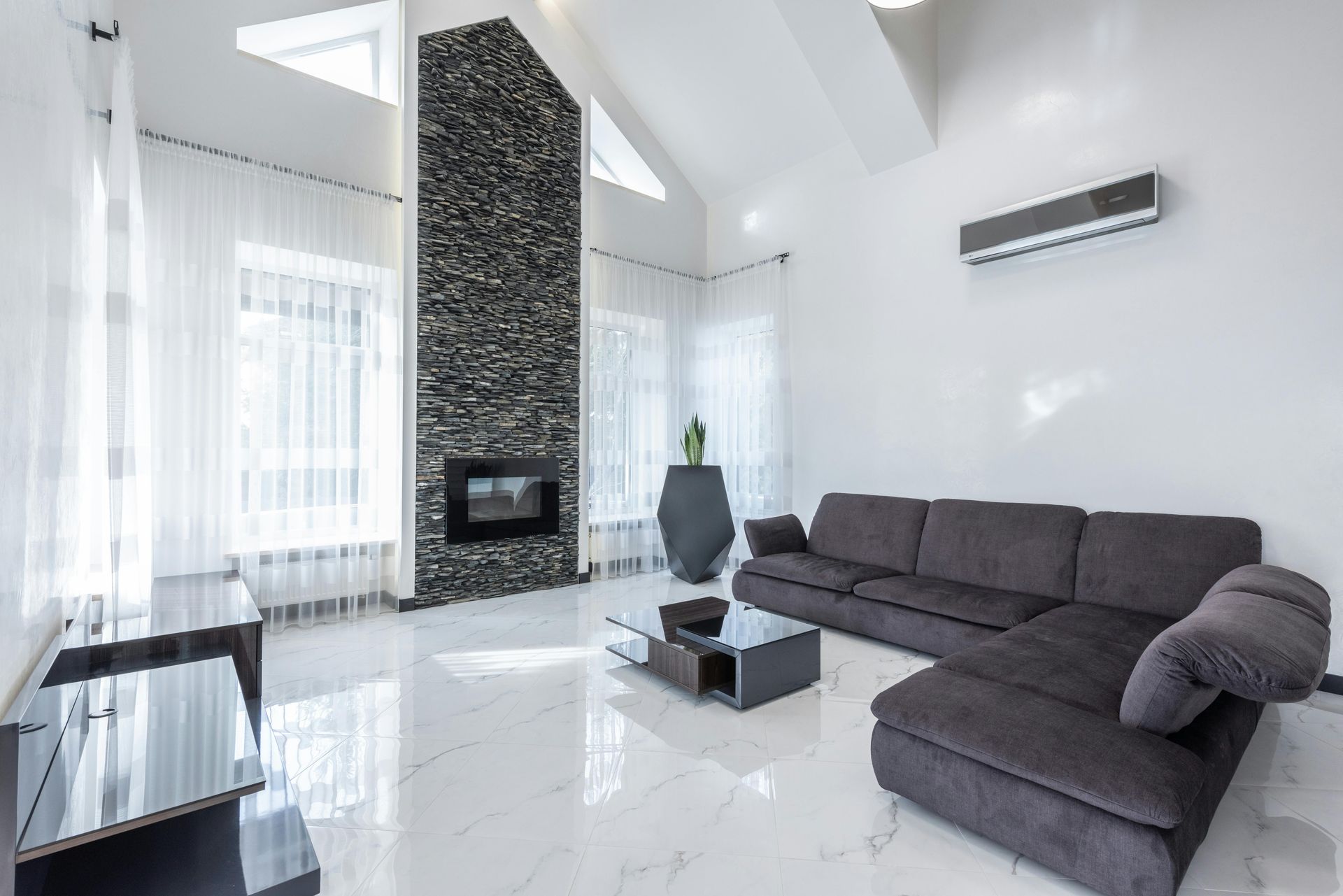 Moderna sala de estar con chimenea de piedra, sofá seccional gris y pisos de mármol blanco.