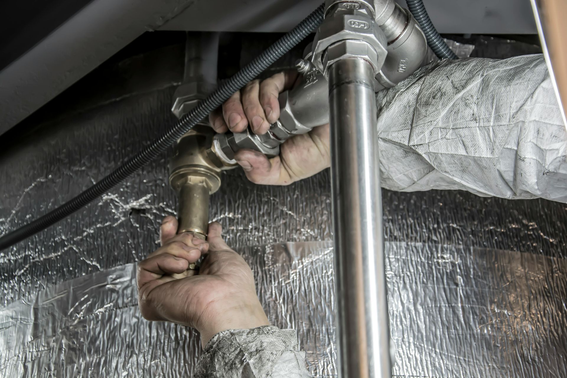 Manos de un fontanero conectando tuberías de metal en un entorno industrial.