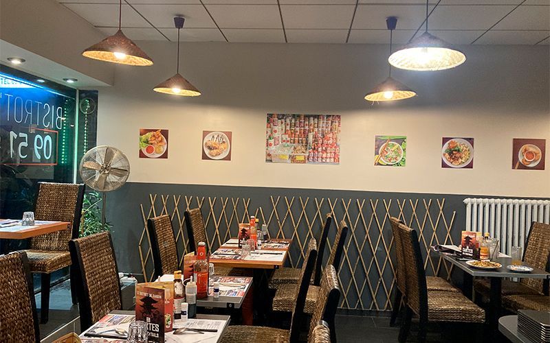 Intérieur d'un restaurant avec tables, chaises et suspensions. Décoration murale avec photos encadrées de plats.