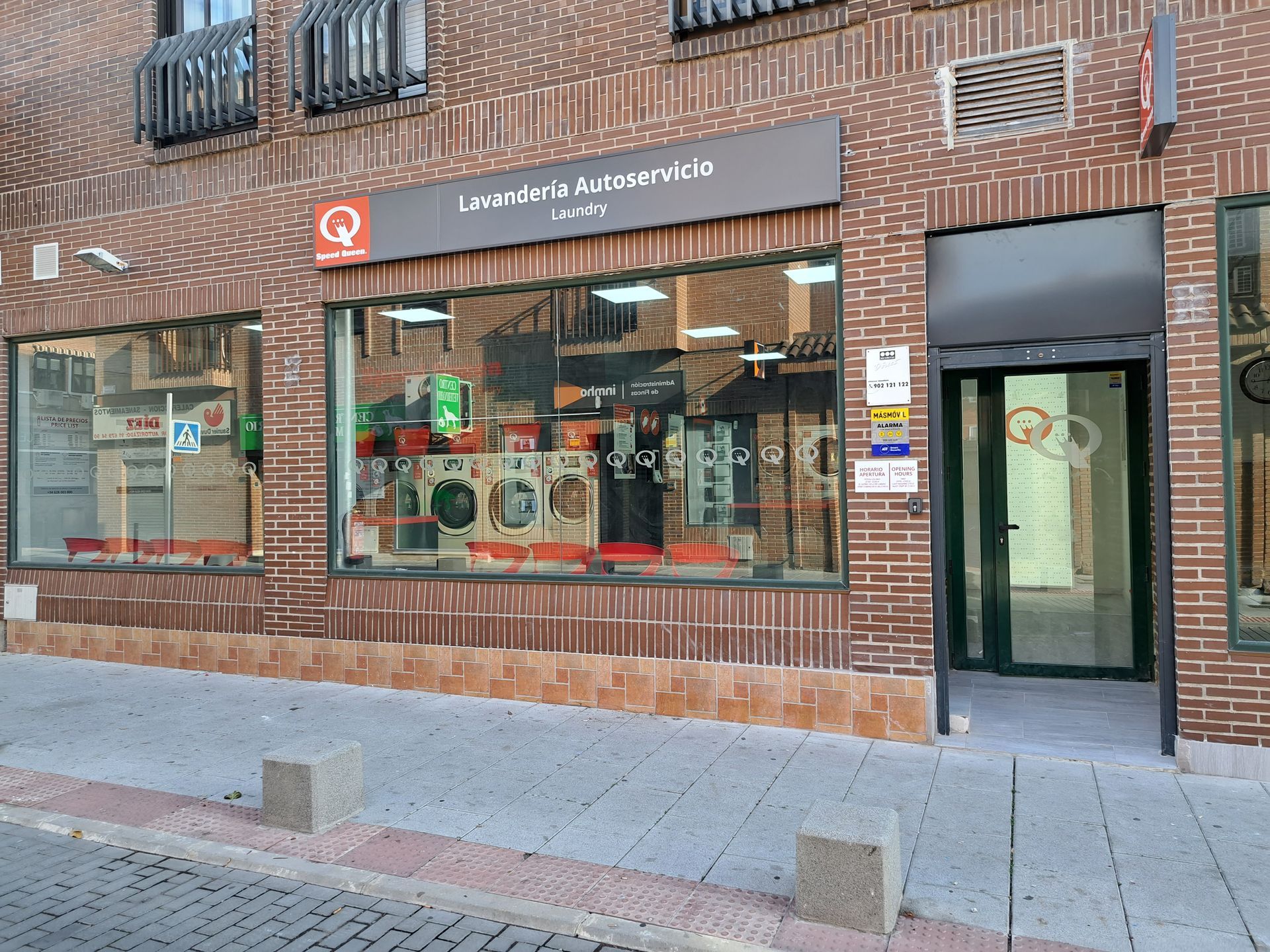 Vista a nivel de calle de una lavandería de autoservicio con un letrero rojo, grandes ventanales y fachada de ladrillo.