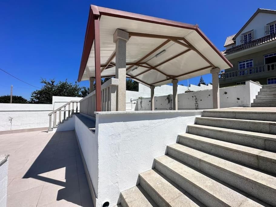 Un pabellón cubierto con columnas de granito, paredes blancas y escaleras bajo un cielo azul.