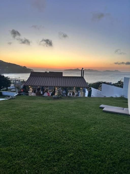 Vista del atardecer sobre un pabellón costero con una reunión en un césped cubierto de hierba.