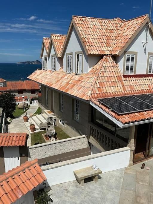 Edificio de varios pisos con techo de tejas rojas, paneles solares y vista al mar en un día soleado.