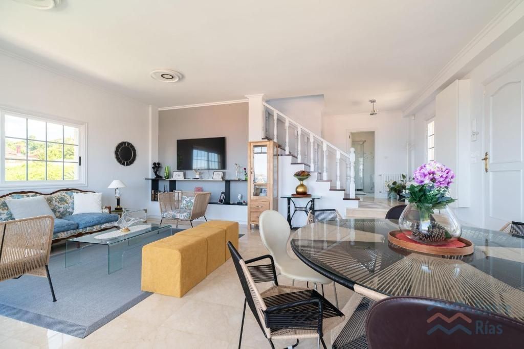 Sala de estar y comedor luminoso y abierto con muebles modernos, escalera y gran ventanal.