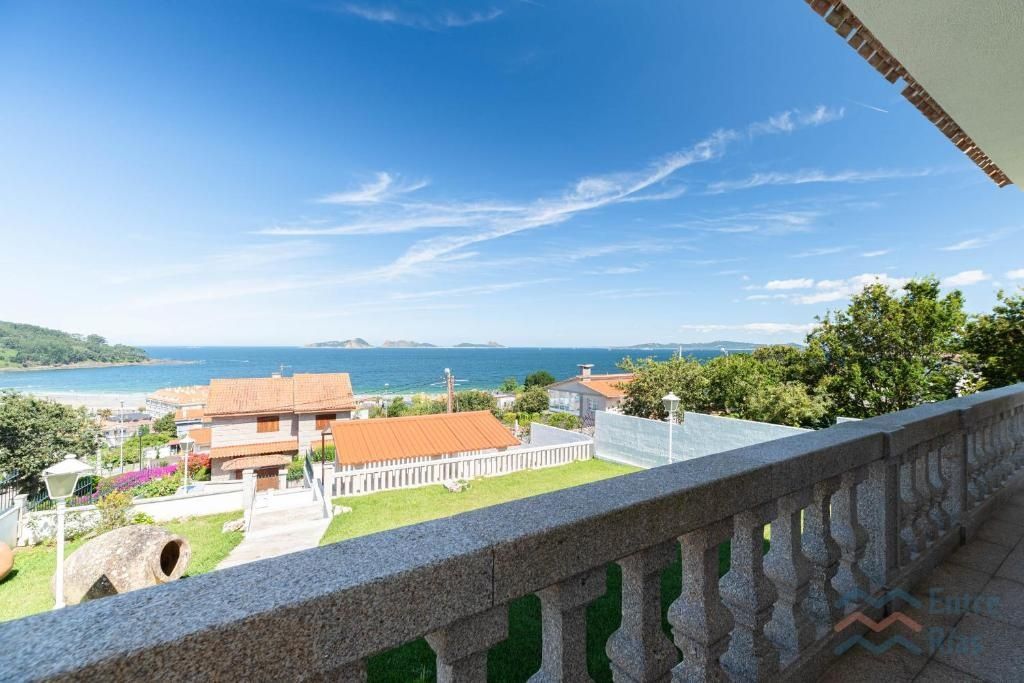 Balcón con vista al mar, cielo azul, edificios, árboles y horizonte nublado.