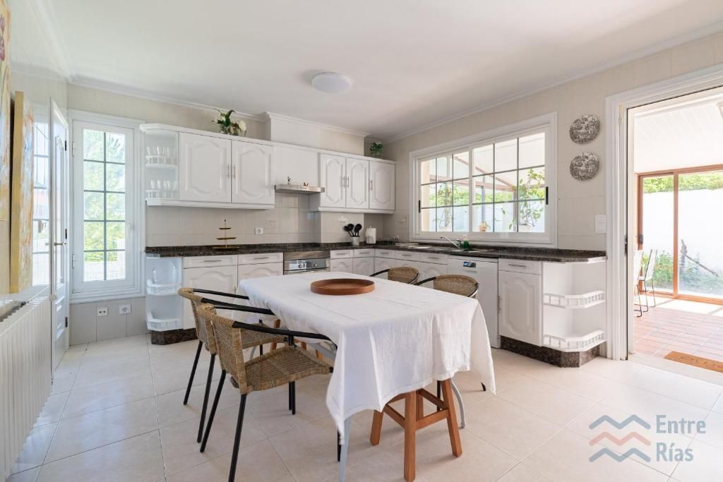 Cocina luminosa con gabinetes blancos, mesa con mantel blanco y puerta abierta al patio.