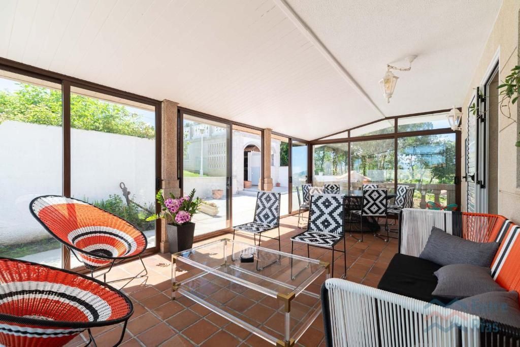 Terraza acristalada con sillas tejidas en tonos naranjas y blancos, mesa de centro de cristal y muebles de patio.