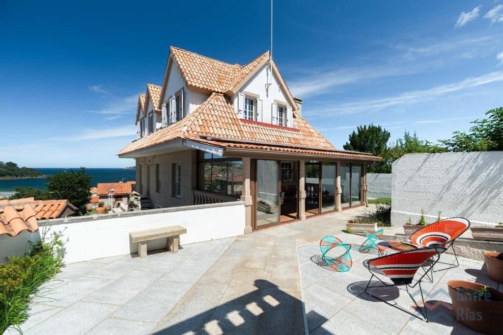 Casa con techo de terracota, patio acristalado y asientos al aire libre con vista al mar en un día soleado.