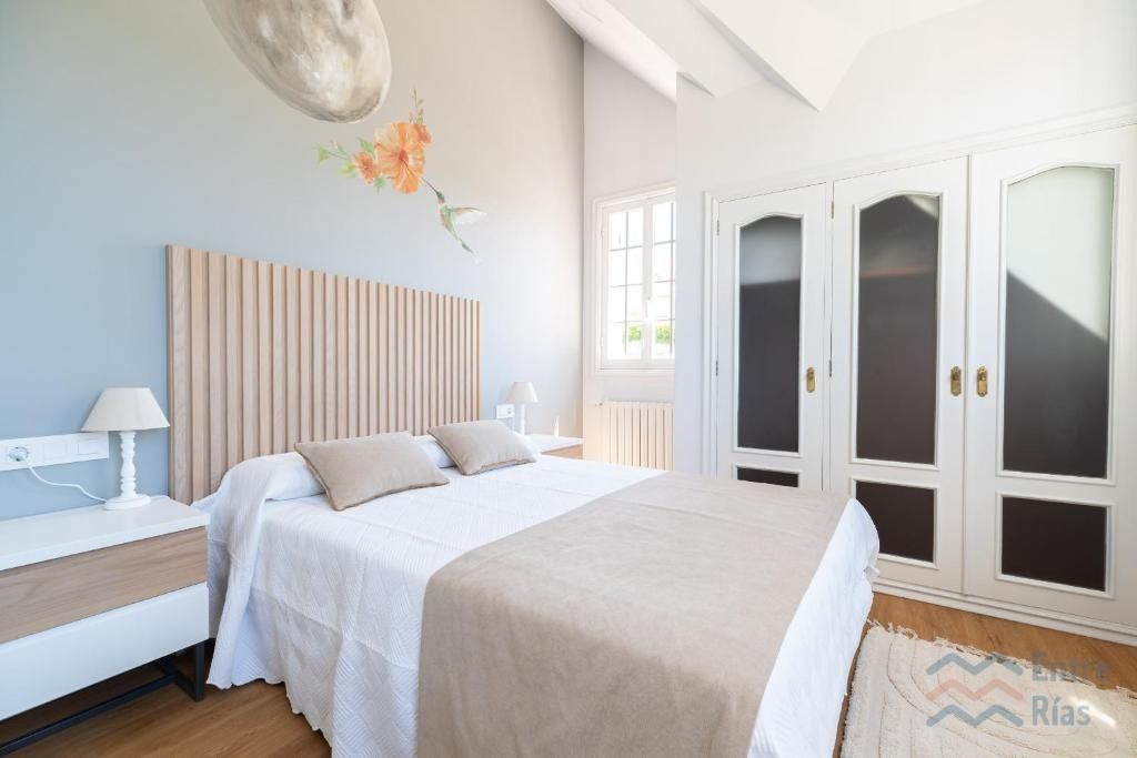 Dormitorio con cama blanca, cabecero beige y un amplio armario blanco. Paredes azul claro con arte floral.