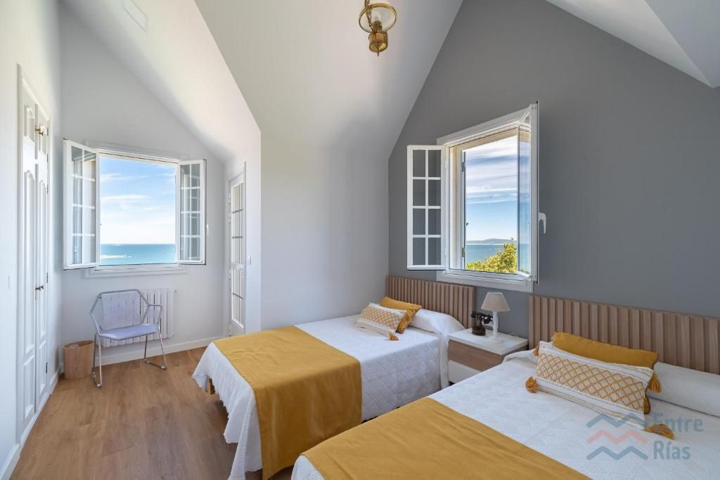 Dormitorio con dos camas individuales, paredes grises y ventanas con vista al mar.