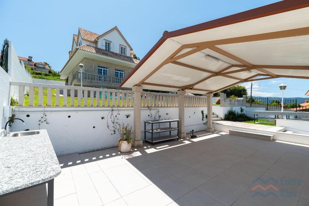Patio al aire libre con zona de estar cubierta, fregadero y vistas a una casa y al océano.