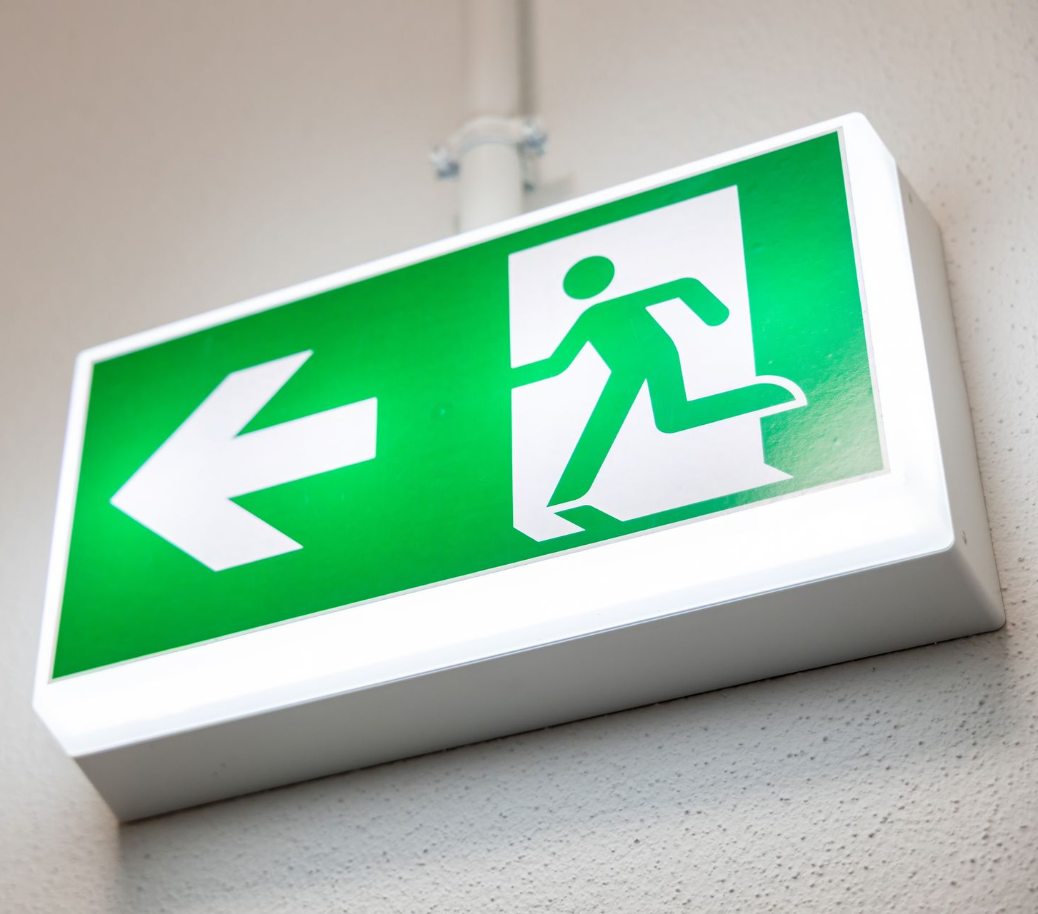 Panneau de sortie vert et blanc ; éclairé avec une personne courant vers une porte ouverte et une flèche pointant vers la gauche.