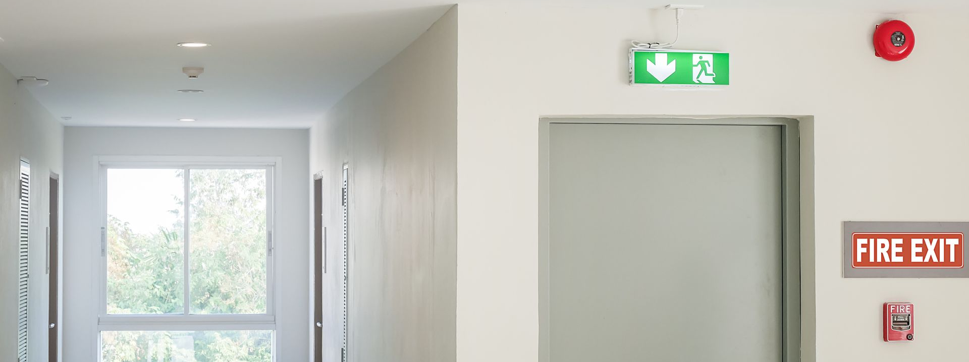 Couloir avec signalisation de sortie de secours et détecteur de fumée.