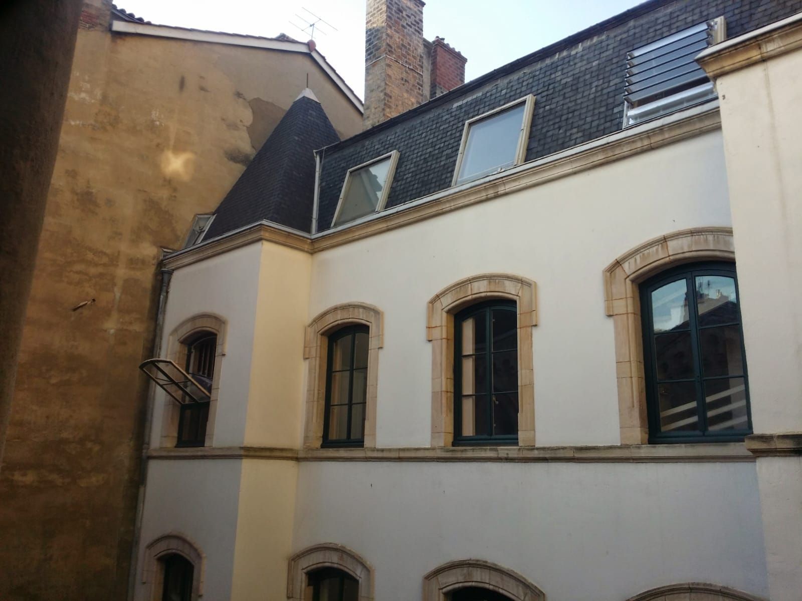 Bâtiment blanc au toit noir et aux fenêtres ornées de pierres apparentes. Vue extérieure.