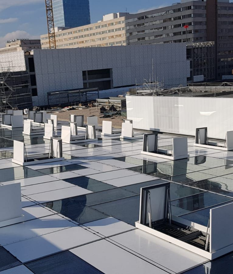 Un toit orné d'un motif en damier de panneaux blanc et gris, avec de nombreuses structures de ventilation blanches. À l'arrière-plan, des bâtiments et une grue de chantier.