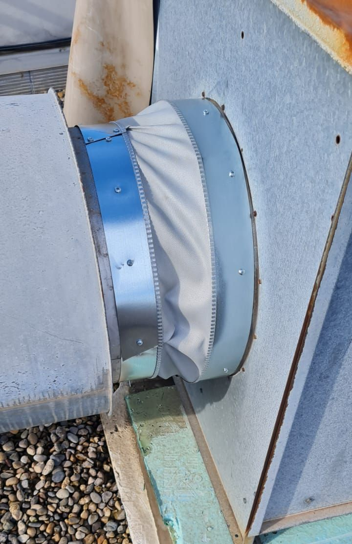 Raccord de conduit flexible sur un toit, avec bandes métalliques argentées et matériau flexible blanc.