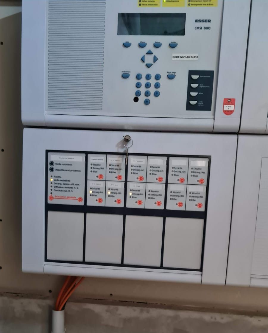 Panneau de contrôle d'alarme incendie avec voyants allumés et clé insérée.