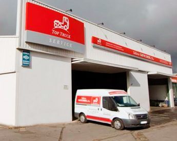 Una camioneta blanca está estacionada frente a un edificio que dice 