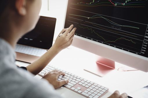Persona analizando gráficos bursátiles en una computadora, señalando la pantalla mientras escribe en un teclado.
