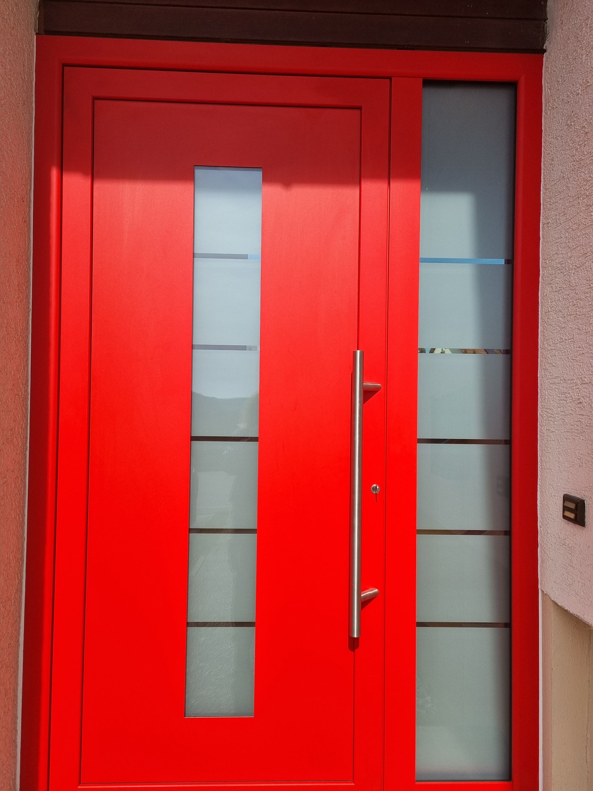 Rote Haustür mit Milchglasscheibe und Seitenfenster, silberner Türgriff.